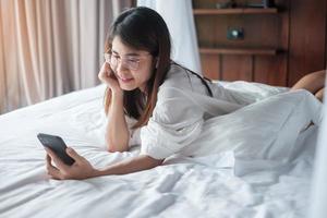 woman using smartphone for social media, young female watching movies by mobile phone on bed at home. technology, network, online shopping, e commerce, lifestyle and digital communication concept photo