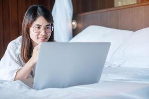 Happy woman using laptop for work, female meeting  online by computer notebook on bed. technology, network, work from home, lifestyle and digital communication concept photo