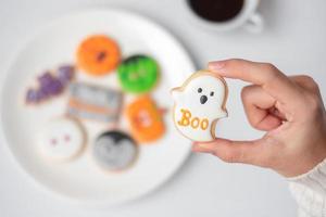 woman hand holding funny Halloween Cookie during drinking coffee. Happy Halloween day, Trick or Threat, Hello October, fall autumn, Traditional, party and holiday concept photo