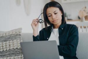 una mujer de negocios enfocada que frunce el ceño trabaja en un proyecto de negocios en una laptop en casa. estrés en el trabajo, horas extras foto