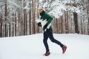 el retrato al aire libre de un hombre positivo y feliz se divierte, camina por el bosque invernal, disfruta de hermosos paisajes y un clima fresco y frío, sostiene un abeto blanco artificial, mira directamente a la cámara. concepto de invierno foto