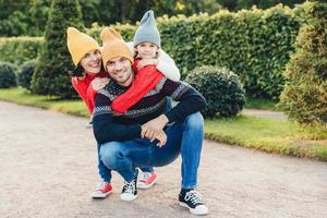 Beautiful female, little girl embrace their handsome father and husband, have good relationship, have active lifestyle, pose against green trees. Family have walk together, embrace each other photo