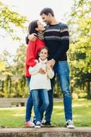 Young happy family of three stand together outdoors, embrace, have good relationships. Couple in love look at each other, hug their little daughter. Happiness and harmony in family life. photo