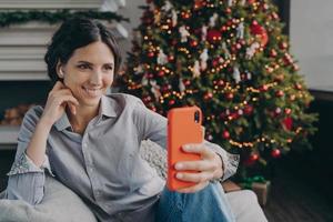 alegre joven española disfrutando de la Navidad en casa, haciendo selfie en smartphone foto