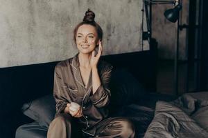 Young pretty european woman in silk pajamas takes care of her skin and body photo