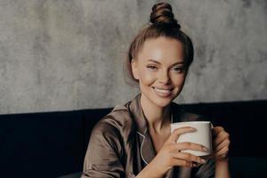 Portrait of young attractive brunette woman with beautiful wide smile drinking coffee in bed photo