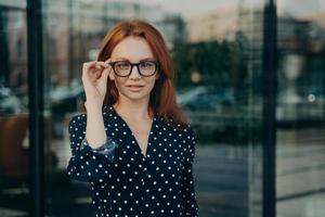 Beautiful redhead woman poses near office building against blurred background photo