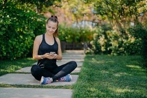 la mujer deportiva tiene un descanso para refrescarse revisa los mensajes y las notificaciones comparten contenido sobre fitness al aire libre vestida con ropa activa lleva un estilo de vida saludable se relaja después del entrenamiento cardiovascular activo foto