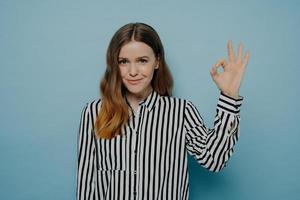 Confident smiling young girl in stripy blouse showing okay sign photo