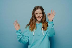 Happy young girl showing okay sign posing over blue blue background photo