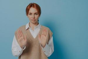 Displeased young 30s red haired woman showing NO gesture, isolated on blue background photo