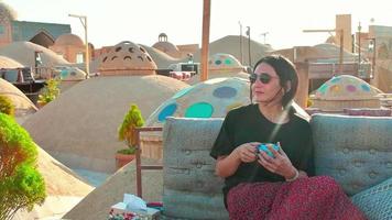 yazd, iran, 2022 - une femme caucasienne boit du café persan dans un café traditionnel sur le toit se détendre profiter d'une vue panoramique sur la vieille ville video