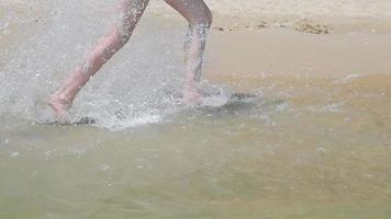 as pernas da menina que correm à beira-mar e formam salpicos e gotas de água. correndo na praia de areia. video