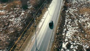 Car riding on winter road with snow in countryside nature in winter. Aerial view from above of auto moving on sunlit roadway with road fork ahead, in frosty morning. Concept of travelling video