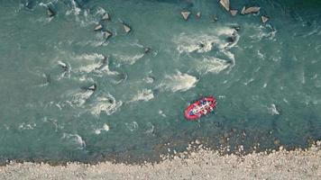 Above view of red inflatable boat drifting through thresholds and stones, rafting on mountain river. Aerial view from drone of group of people rafting in rubber dinghy at daytime. Concept of rafting video