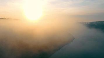 fantastiskt landskap av dimmig flod i soliga strålar. Flygfoto från drone of mystery valley med slingrande dimmig flod som flyter mellan kullar med vacker solnedgång i bakgrunden. begreppet landskap video