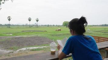 mujer asiática leyendo un libro y bebiendo café mientras toma vacaciones en el campo video