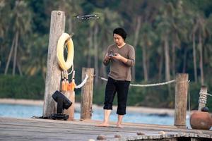 Asian man concentrate to controls and monitors drone on the sea jetty. photo