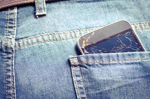 Broken cell phone in a back pocket. Jeans background with a broken smartphone. photo