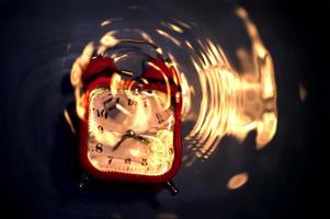 Blurry abstract composition with drowning alarm clock and ripples with fire reflected on water surface. photo