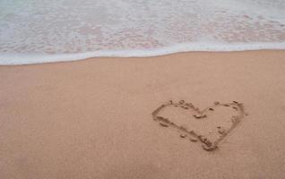 Heart symbol of love hand drawn on sand summer beach. photo