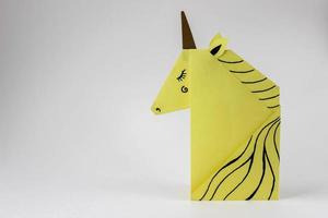 Yellow unicorn made in the origami technique on the right side of the photo on a white background. With place for your text.