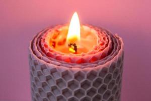 Cierra la vela de cera encendida sobre fondo rosa. foto