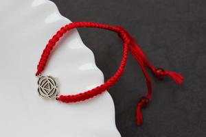 Orange handmade braded bracelet with chakra muladhara on the edge of a snow-white plate photo