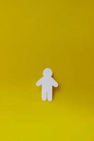 Silhouette of a man of white paper, cut by hand on yellow background. Vertical photo with copy space