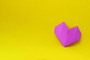 corazón de origami de papel púrpura sobre un fondo amarillo en el lado derecho de la foto. fondo minimalista con espacio de copia foto