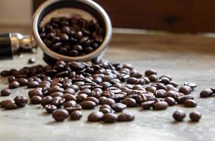 granos de café arábica marrones esparcidos sobre una mesa de hormigón con un enfoque suave en el soporte del filtro. enfoque selectivo en el término medio foto