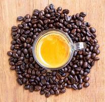 top view of a cup of hot espresso coffee with a nice crema on a wooden table surrounded by a pile of brown roasted coffee beans. selective focus on cup of coffee photo