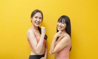 Portrait of healthy and slim Asian athlete women in sportswear smiling on the isolated yellow background for exercise and workout photo