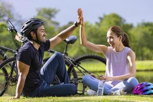 joven pareja asiática dando cinco después de andar en bicicleta en el parque público para actividades de ejercicio de fin de semana y concepto de búsqueda recreativa