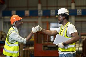 Team of African American industrial worker is doing fist bump while working inside roof factory for agreement and safety industry concept