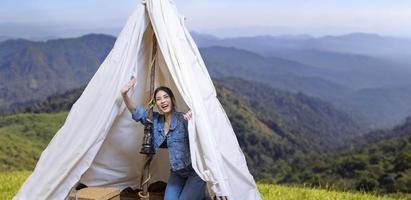 Asian woman greeting friend while on a solo trekking camp on the top of the mountain with small tent for weekend activities and outdoor pursuit concept photo