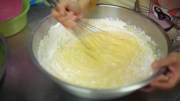 With an immersion blender with a whisk, the girl beats dough in a metal pot. The process of making a dough for home baking. Cooking pie, cookies, pizza at home in the kitchen. video