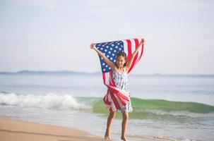 Happy kid girl playing on the beach and holding USA flag, Child girl raising United States of America flag photo