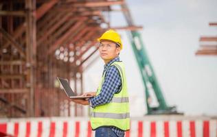 Engineer checking project at the building site, Man in hardhat with laptop at the infrastructure construction site photo