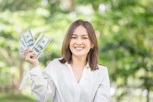 Smiling young freelancer relaxing and holding money banknotes blurred green background, Happy woman holding and showing money banknotes photo
