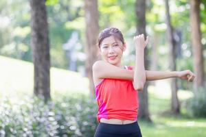 fitness mujer estirando los músculos antes de la actividad deportiva, mujer gimnasio en el parque ejercicio matutino, joven deportista haciendo ejercicio estira la mano y preparándose para correr foto