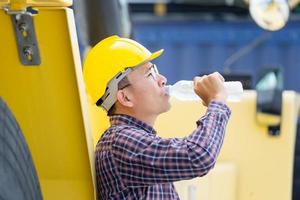 Worker man in hard hat drinking water at containers cargo photo