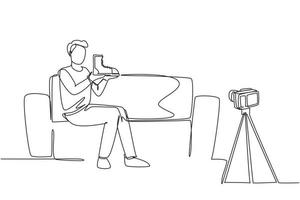 Single one line drawing social media influencer reviewing boots. Smiling young man vlogging about men's sports shoe and filming himself at home on a video camera. Continuous line draw design vector