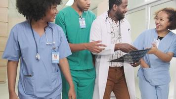 gruppo di professionisti, medico maschio afroamericano professionista con il team di giovani studenti di medicina cammina felice e discute la pellicola radiografica per la diagnosi all'esame clinica sanitaria ambulatoriale in ospedale. video