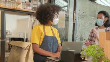 barista afroamericana con mascarilla trabaja en el café con distancia social, café para llevar para un cliente, nuevo servicio normal de cafetería de pequeñas empresas en el estilo de vida de cuarentena covid19. video