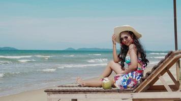 Asain Woman in bikini lying on lounge chair and coconut. Vacation and summer travel video