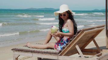 schöne Frau sitzt auf einem Liegestuhl und trinkt. urlaubs- und sommerreisekonzept kokosnuss. video