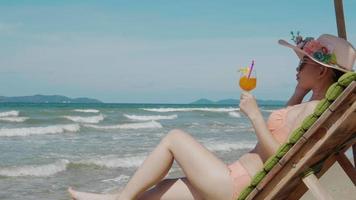 bella mujer sentada en un sillón, bebe jugo de naranja. concepto de viaje de vacaciones y verano video