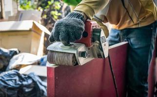 Carpenter is shaving red wood door by his shaving machine in outdoor field with steel pole building structure environment. photo