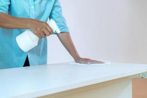 Asain maid worker is cleaning table with anti coronavirus cleanser in foggy before use. photo